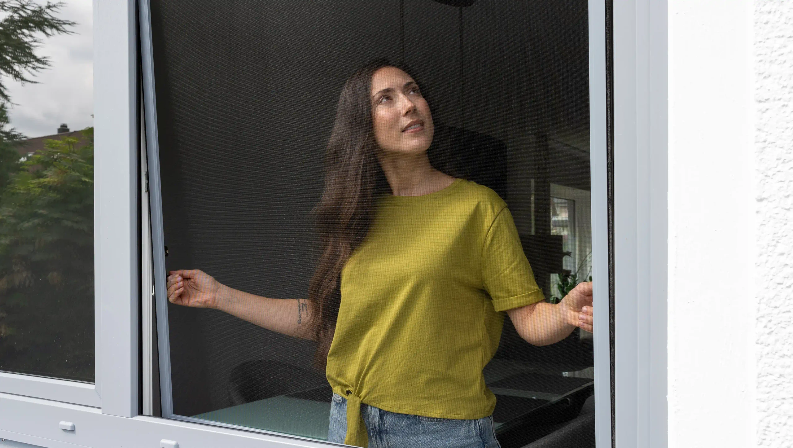 Frau mit grünem T-Shirt kippt ein transparentes Insektenschutzgitter in einem Fenster